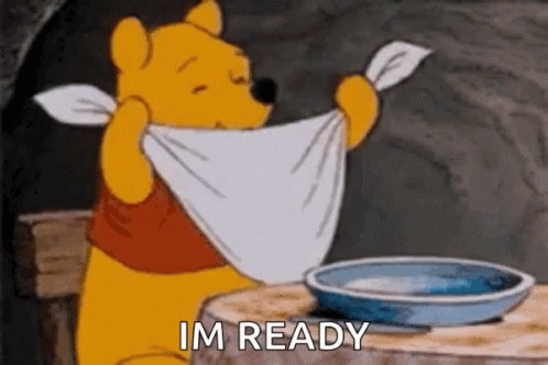 A GIF of Winnie the pooh tying a napkin around his neck and preparing to eat at his table